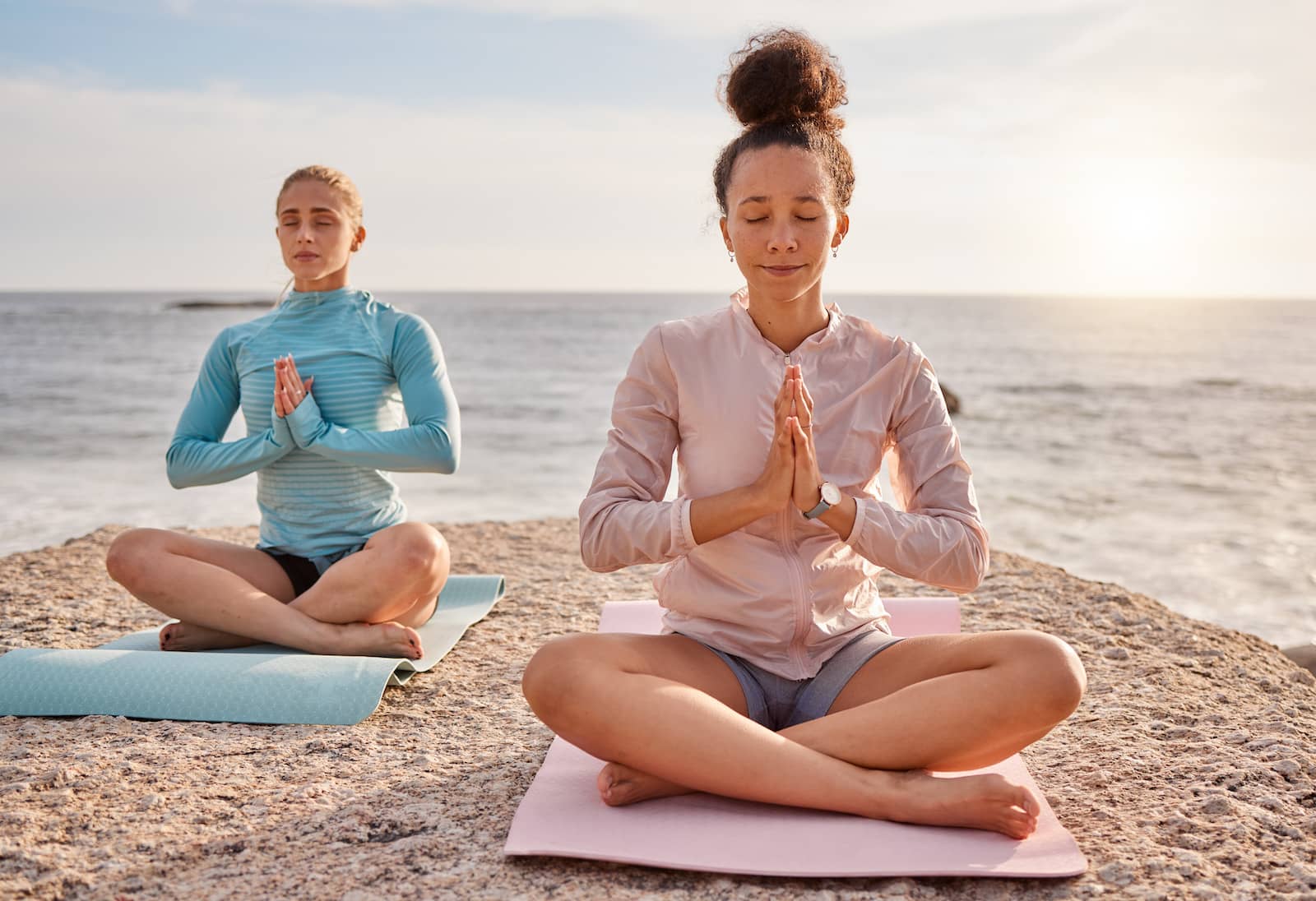 two friends doing yoga on a rock with a beach in the background